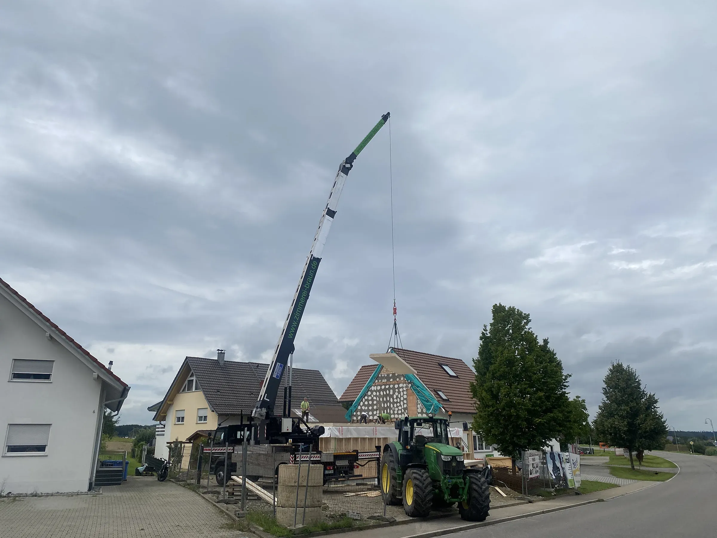 Autokran hebt ein Dachelement über ein Wohnhaus