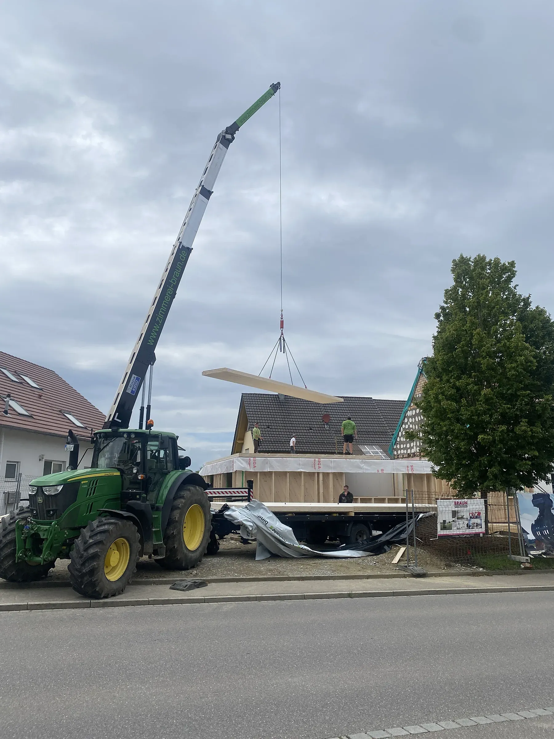 Autokran setzt ein großes Dachbauteil auf einen Neubau
