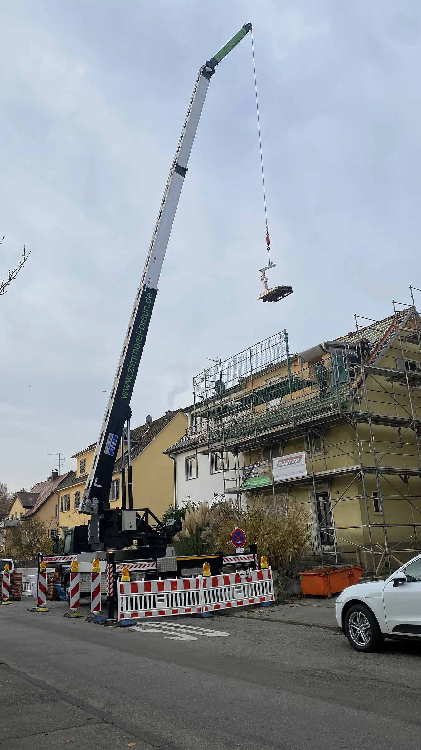 Autokran neben einem eingerüsteten Haus, die Straße ist abgesperrt